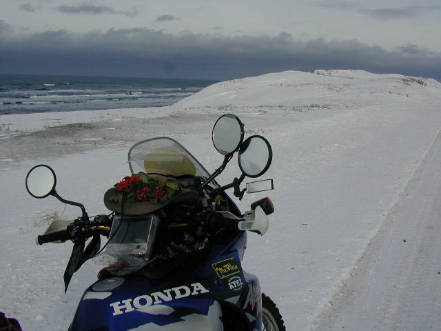 雪に閉ざされた海岸道路に停められた伴走バイクの写真