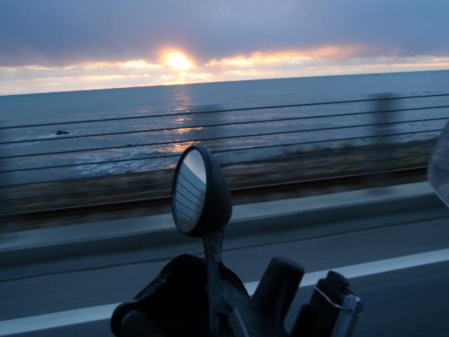 元旦宗谷岬ツーリング2022(エァー)思いを巡る旅_2009年正月日高の海岸線で雲間から太平洋に沈む夕日を追いかけるバイクのバックミラーに映る残像の写真