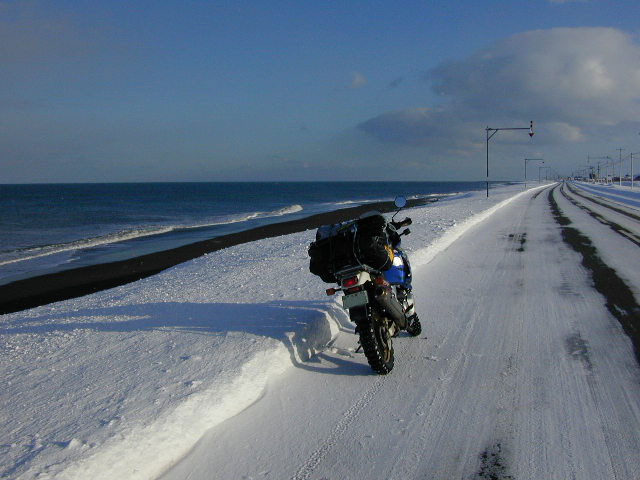 水平線を境に向き合う、空の青と雲の白､海の青と雪の白、美しいコントラストの中を走るバイクの写真