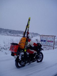 スキーと雪中キャンプ用具を積載して走るバイクの後ろ姿の写真