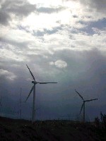 空を覆う雲に光を遮られて暗い地上で黙々と回り続ける巨大風車の写真