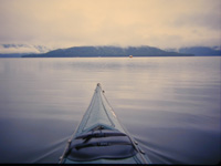 波の無い滑らかな湖面を中心の中島に向かって進むカヌーから見た湖面の風景の写真