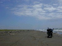 何にもない広い広い砂浜と青空と海の風景の片隅に止まるバイクの写真