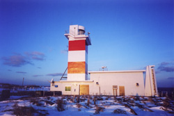 2007年の夜明け、青空の中朝日に照らされて朱色に染まる白い宗谷岬灯台の写真