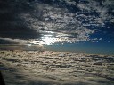飛行機の窓から見る上下二層に分かれた雲間を飛び交う眩しい光の写真