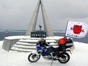 2000年元旦宗谷岬にて日本最北端の碑の前で寄せ書きを施された日の丸国旗をはためかせる伴走バイクの写真