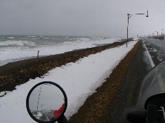 道路脇に帯状に雪が残る海岸線の写真