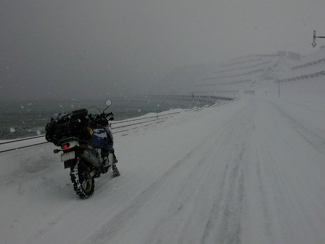 地吹雪に包まれるオホーツク海岸を進むバイクの写真
