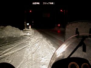漆黒の闇の中に伸びる純白の雪道とその開いている閉鎖ゲートの赤色回転灯の写真