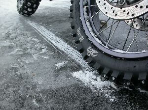 大型バイクのフロントタイヤのスパイクピンがアイスバーンを引っかいて削っている写真