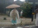雨合羽を着込んで傘をさした神官の後ろを駆け抜けるランナーの写真