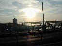 大きな川に幾重にも掛かった橋を全て貫くように光を投げる太陽の写真